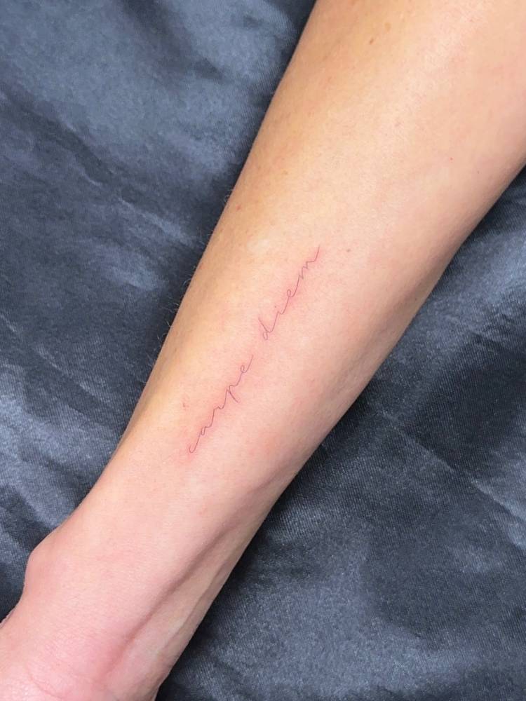 Handwritten font "carpe diem" lettering tattoo located on the wrist.