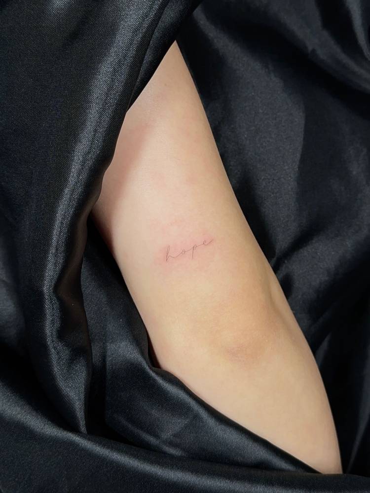 Little tattoo of the word "hope" in handwritten font located on the tricep.