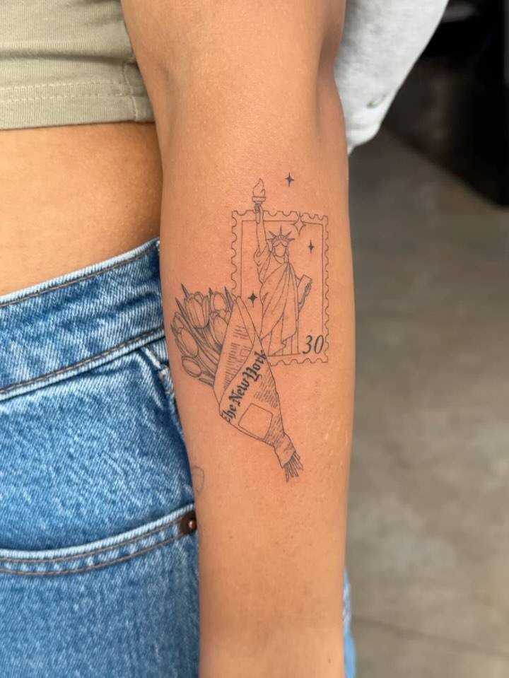 Statue of Liberty stamp and flower bouquet tattoo located on the forearm.