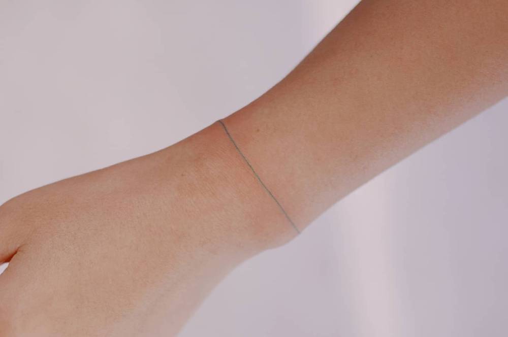 Green ink wristband tattoo in fine line style.