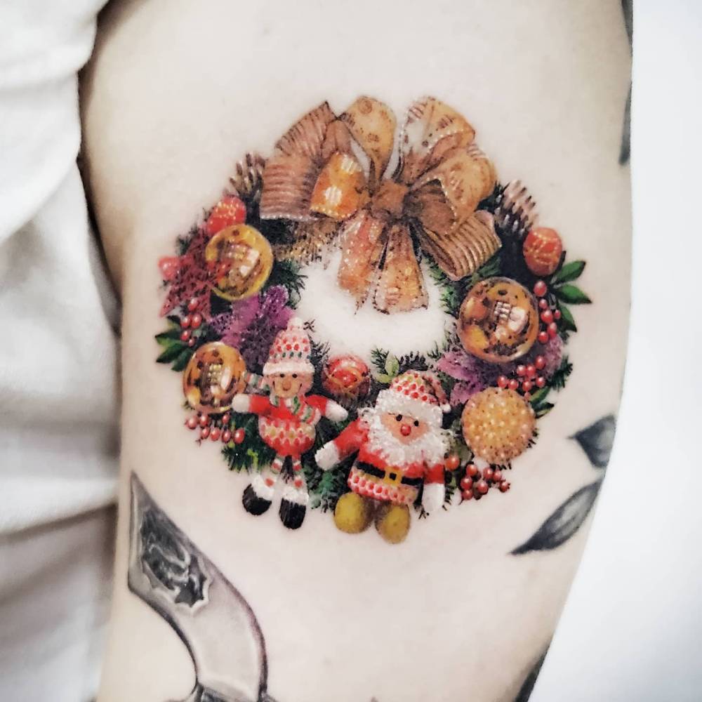 Micro-realistic style Christmas wreath tattoo located on the upper arm.
