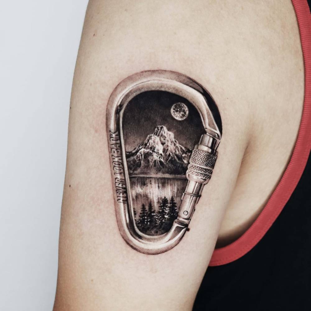 Micro-realistic style carabiner clip and mountain tattoo located on the upper arm.