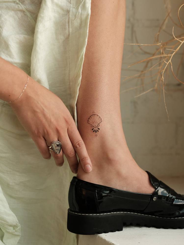 Fine line style ornamental scallop shell tattoo located on the ankle.