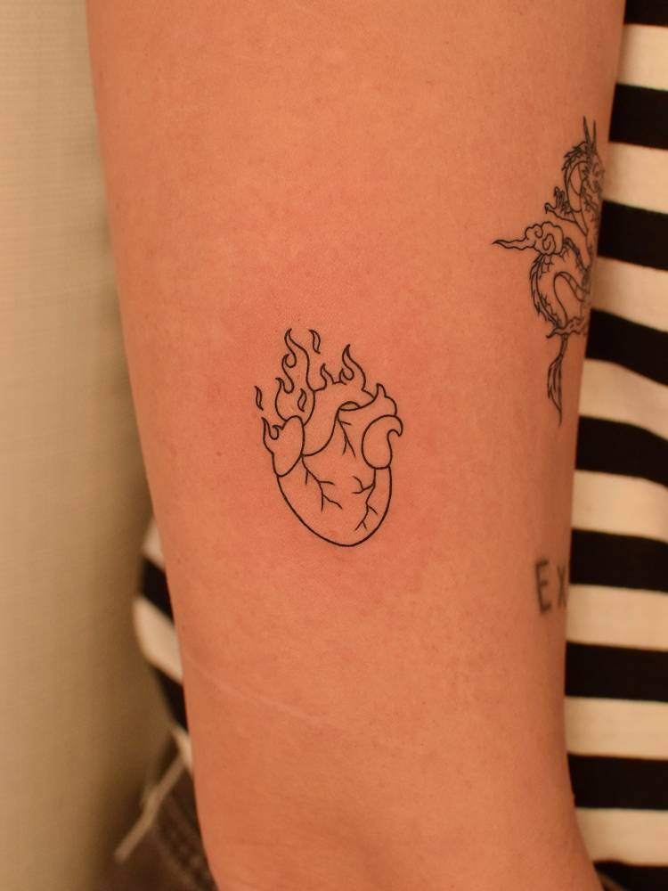 Flaming anatomical heart tattoo located on the upper arm.