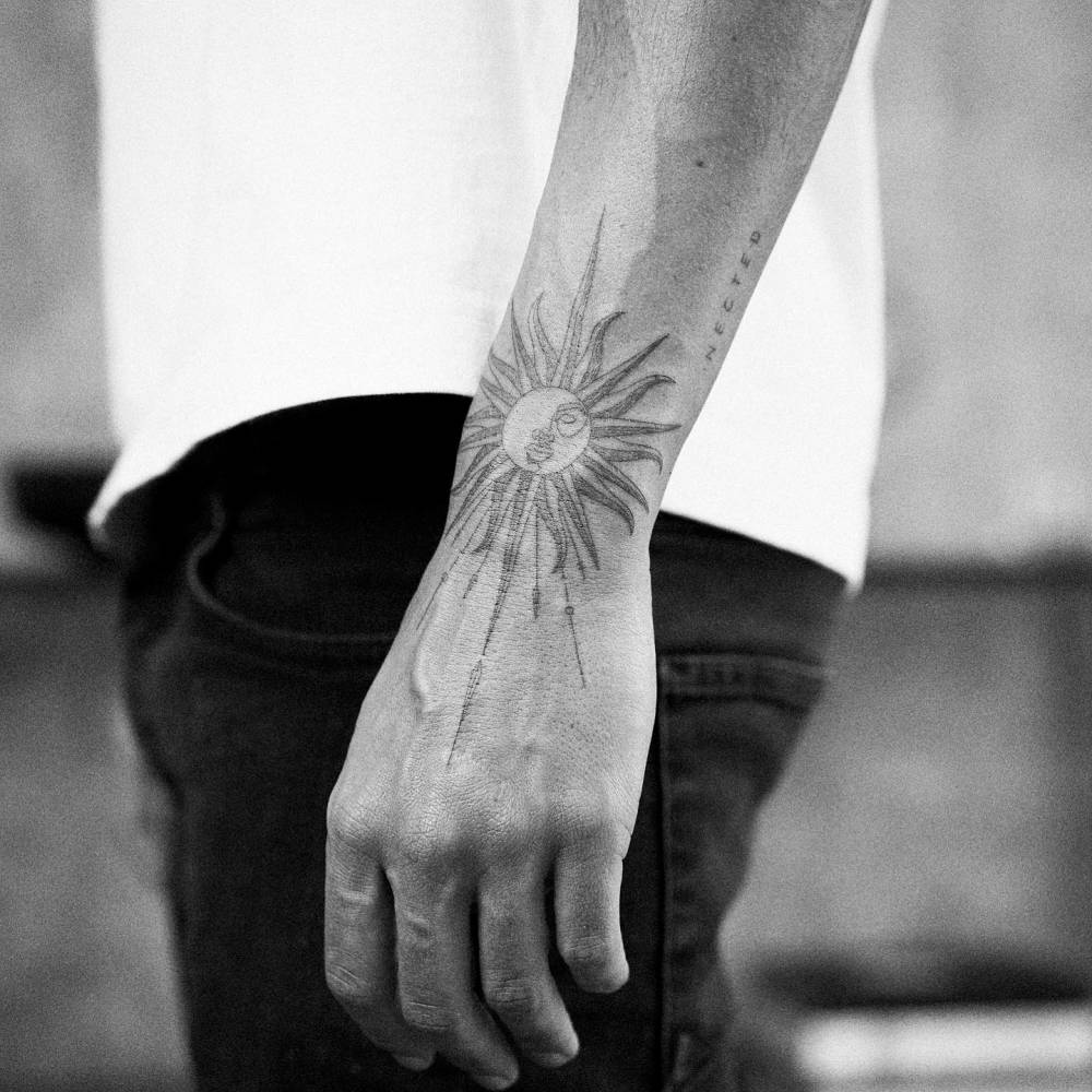 Sun tattoo located on the wrist, illustrative style.