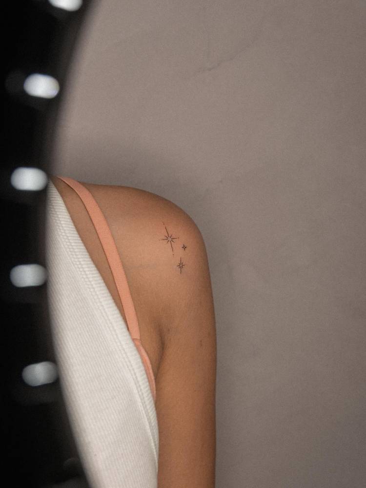 Sparkling stars tattoo in fine line style located on the shoulder.