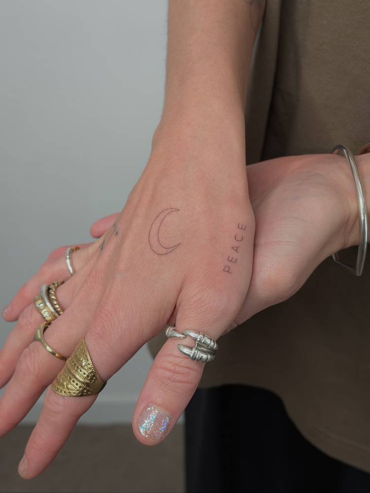Crescent moon and word "peace" tattooed on the hand.