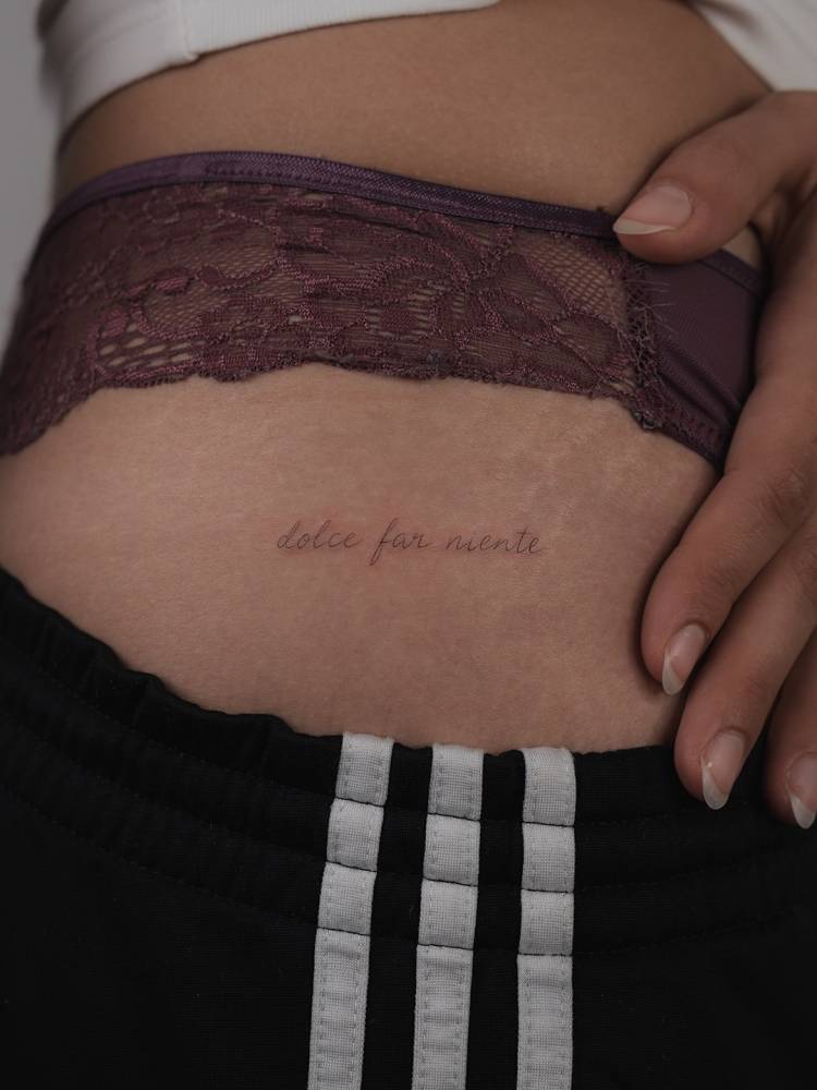 "Dolce far niente" lettering tattoo located on the hip.