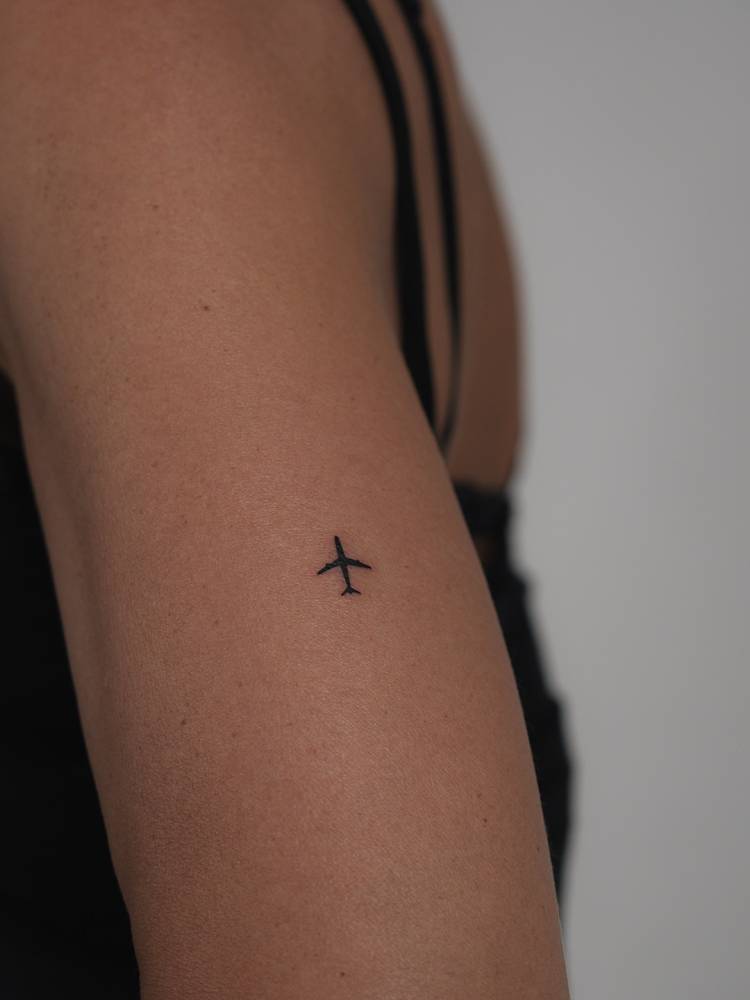 Tiny minimalistic airplane tattoo placed on the tricep.