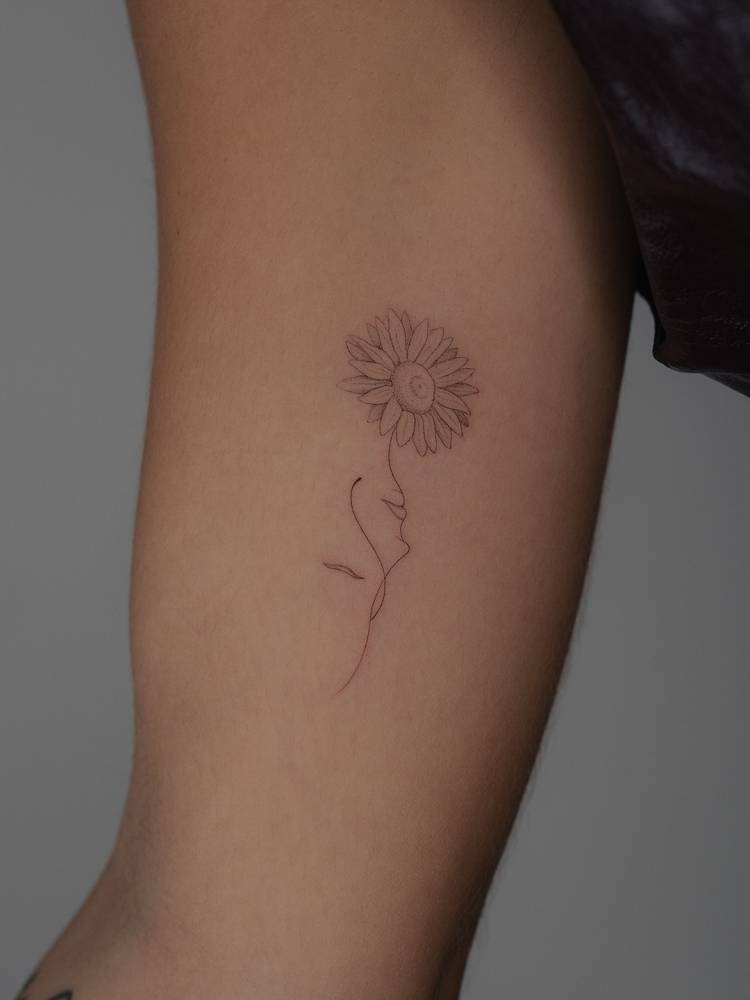 Single needle flower head woman tattoo located on the inner arm.