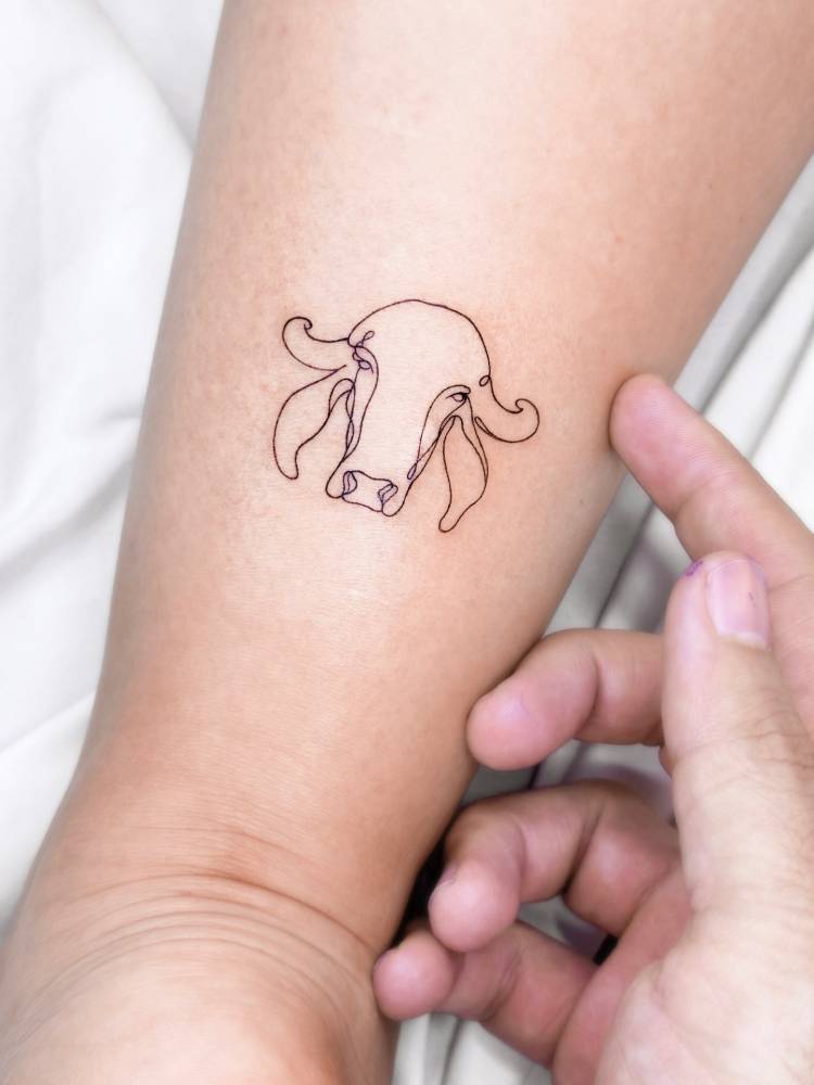 One line cow head tattoo located on the achilles.