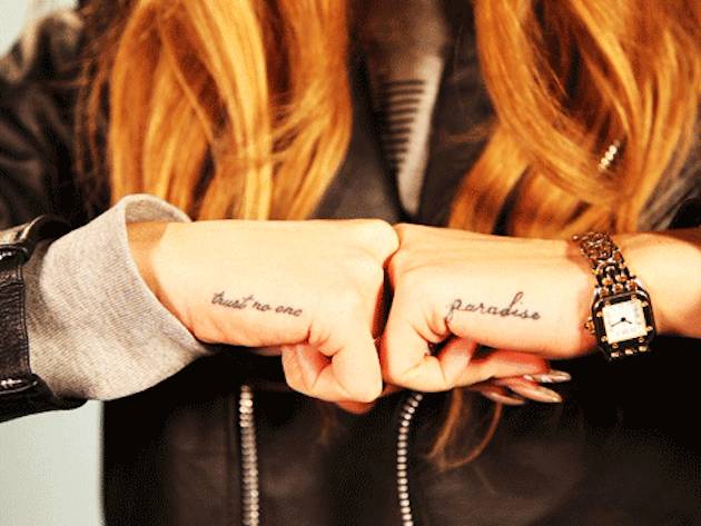 "Trust no one" and "paradise" lettering tattoos located on Lana Del Rey's hands.