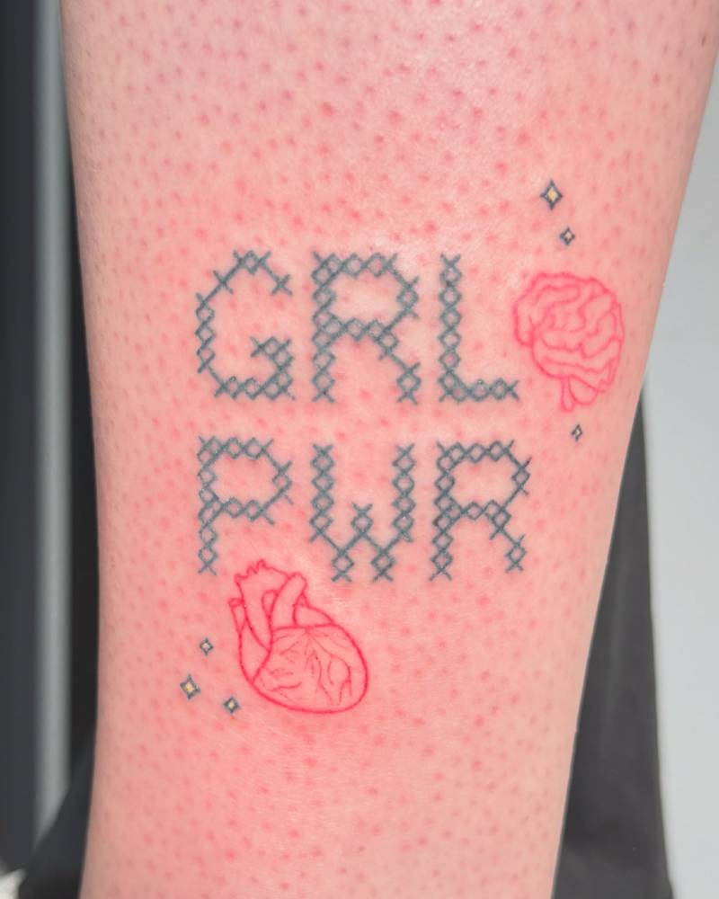 Cross stich lettering tattoo that says "grl pwr" located on the ankle.