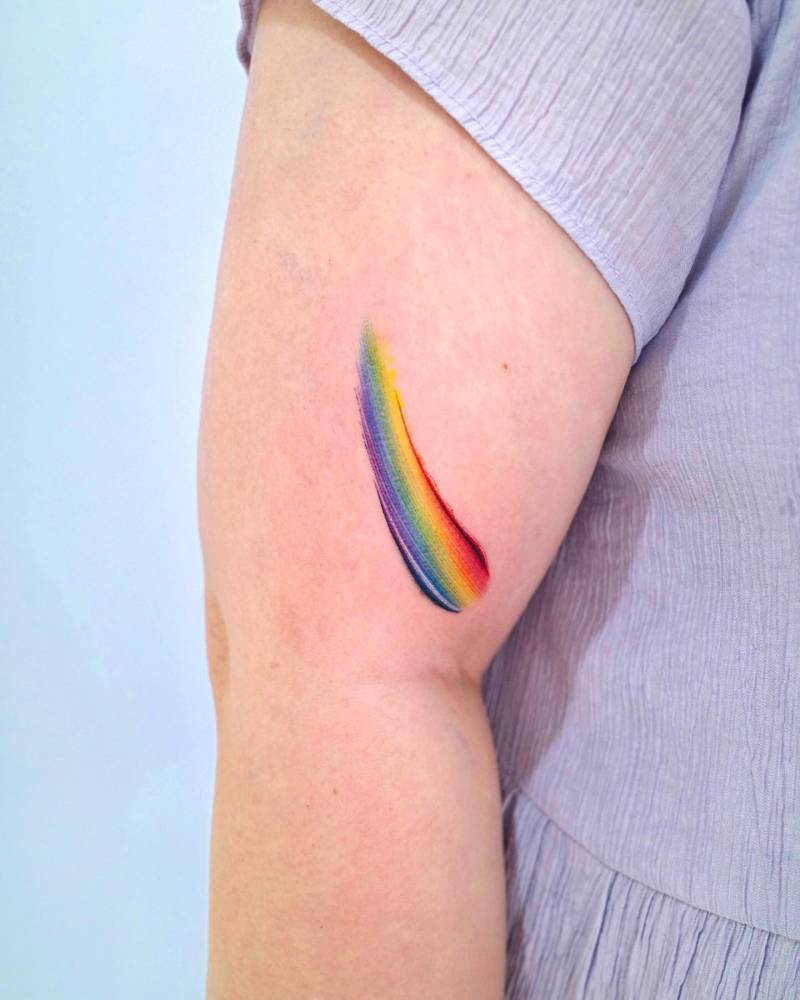 Watercolor style visible spectrum brush stroke tattoo located on the upper arm.