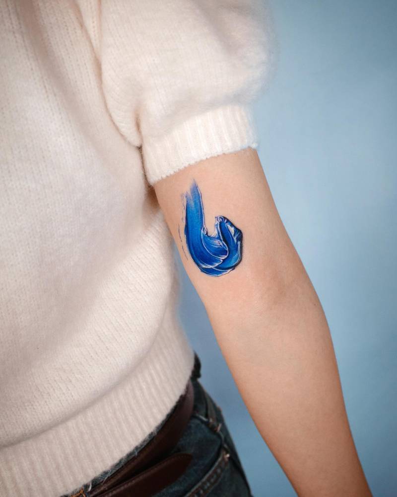 Blue brush stroke tattoo placed on the inner arm, realistic style.