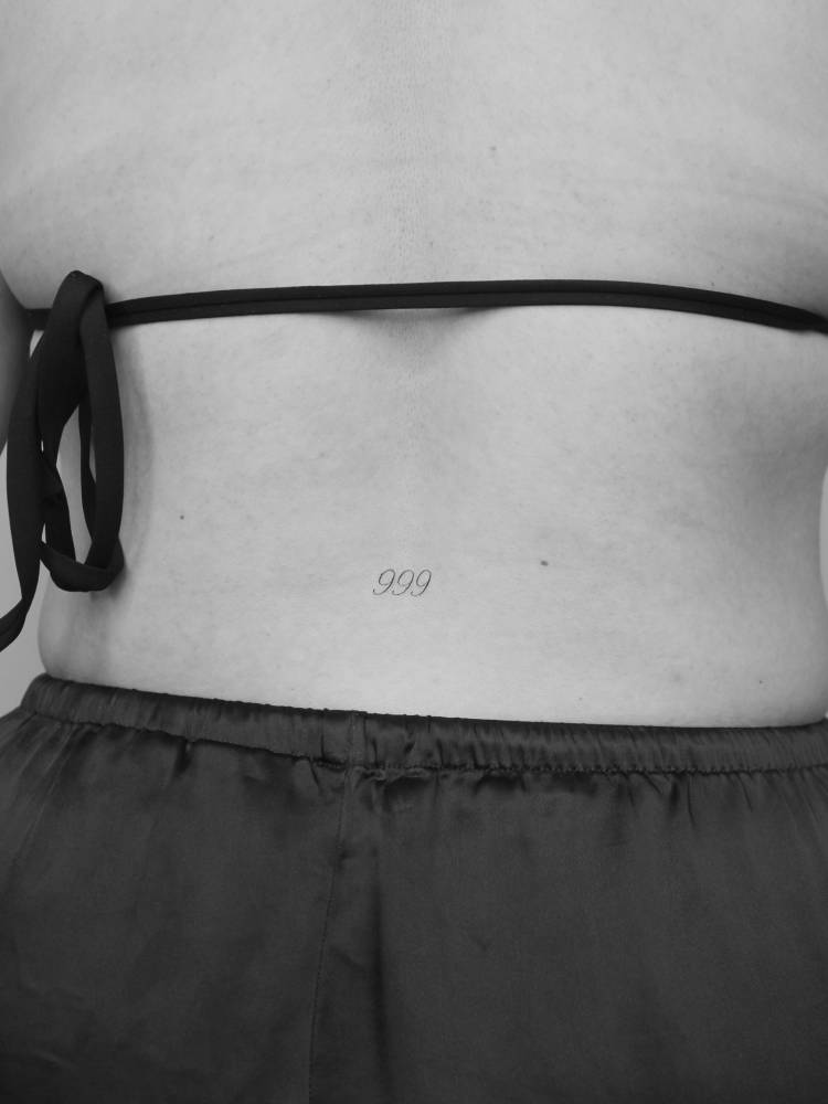 Angel number "999" tattoo located on the lower back.