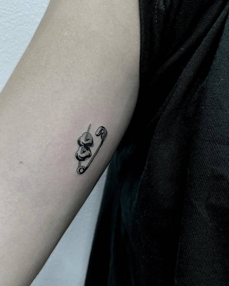 Safety pin and hearts tattoo located on the inner arm.