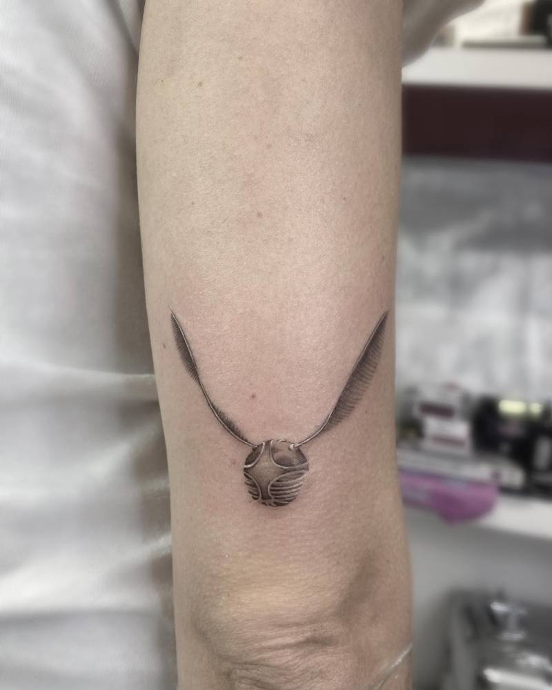 Golden snitch tattoo in micro-realistic style located on the tricep.