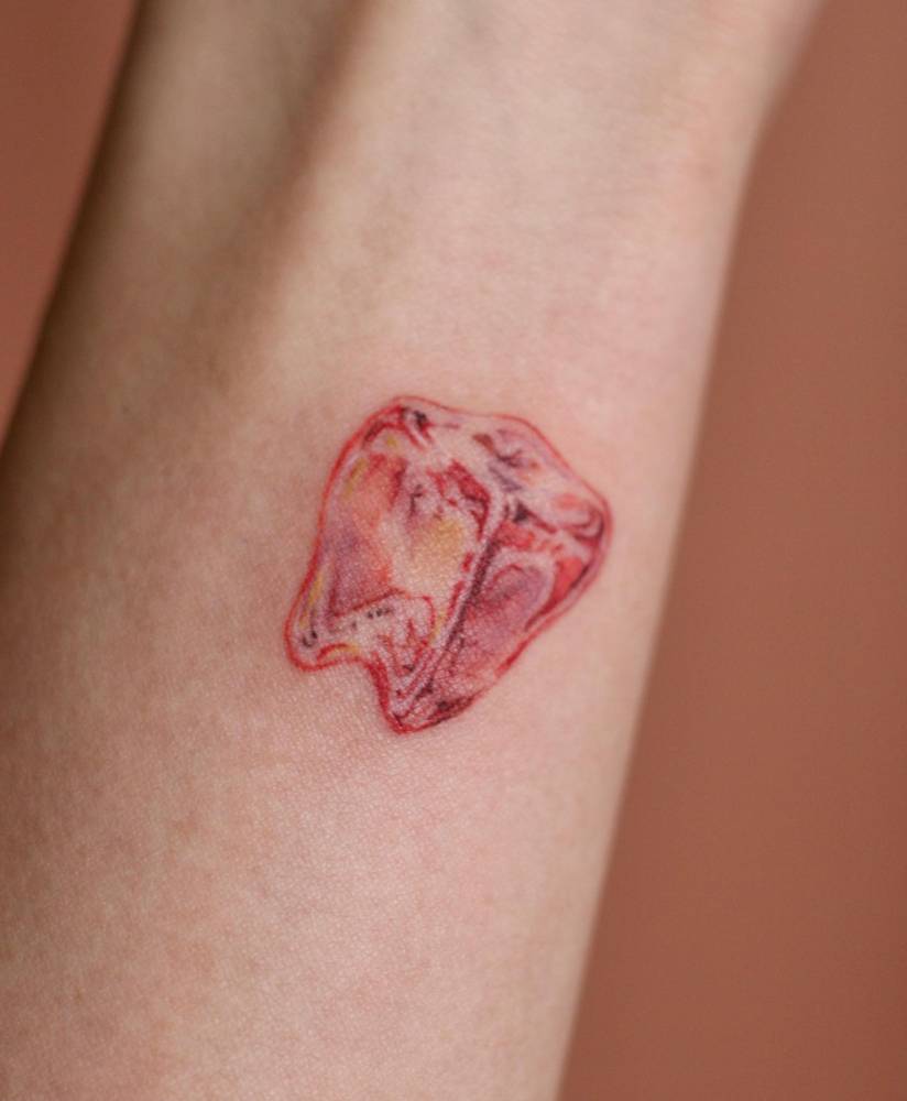 Red transparent tooth tattoo located on the wrist.
