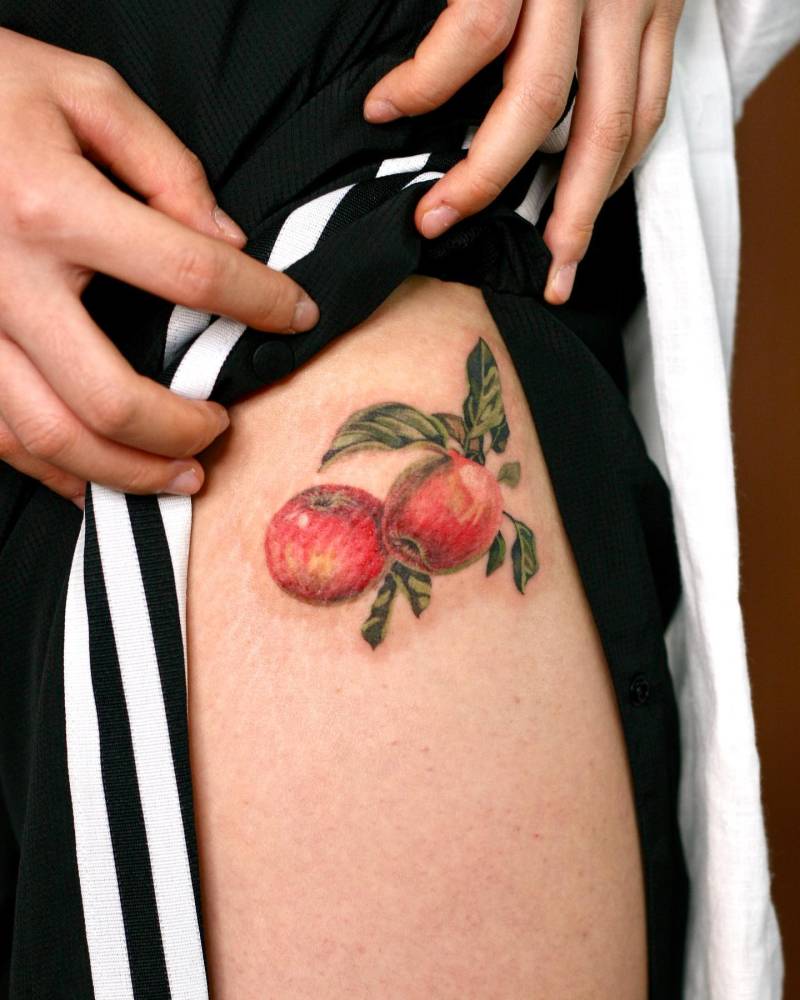 Watercolor style apples tattoo located on the thigh.