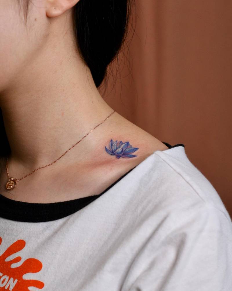 Watercolor style lotus flower tattoo located on the collarbone.