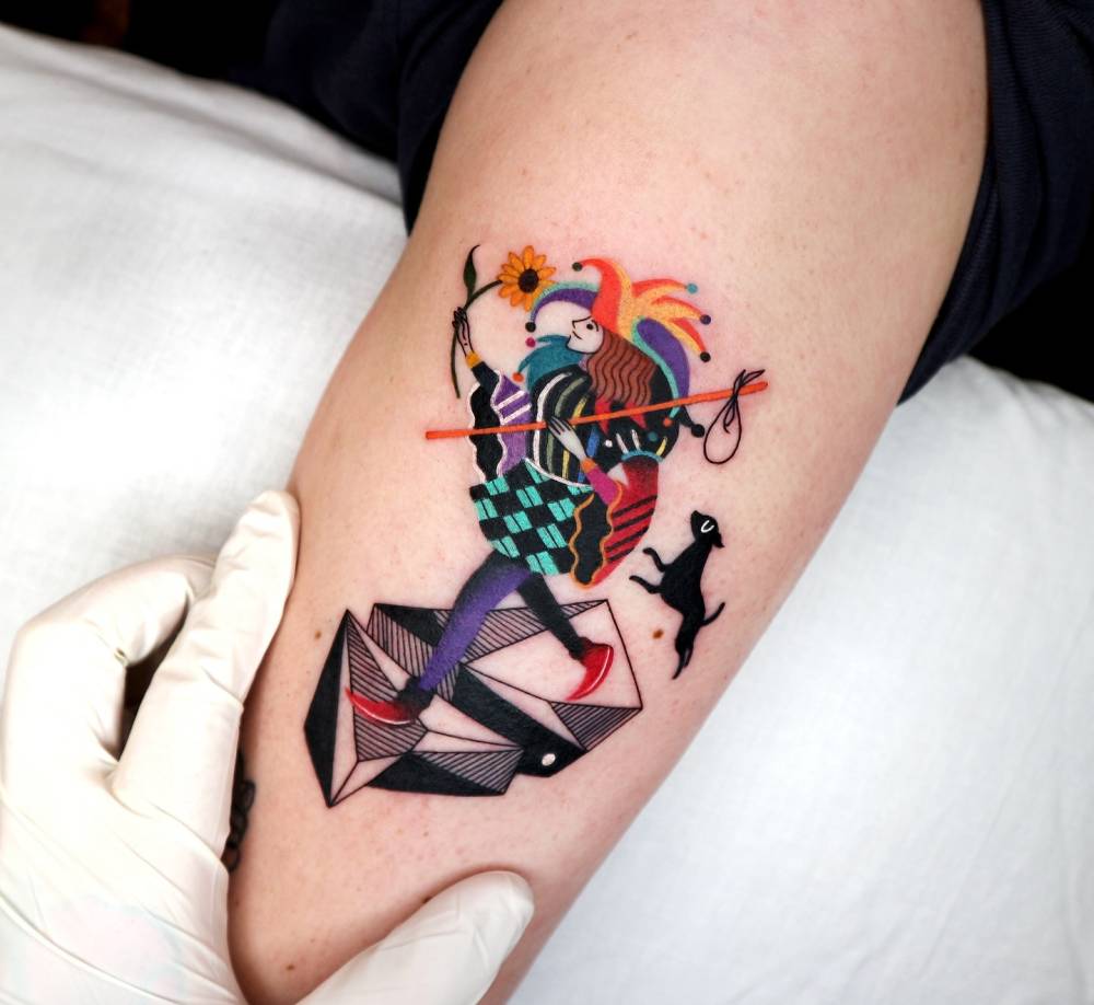 Pop art style The Fool tarot card tattooed on the upper arm.