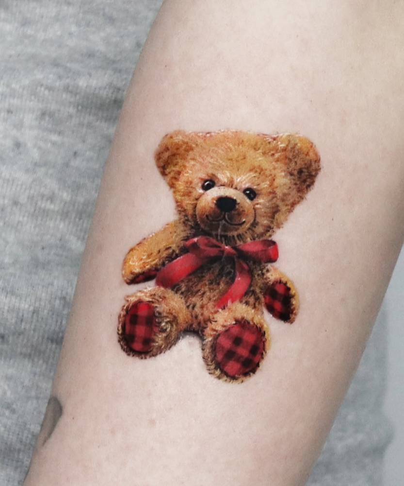 Micro-realistic style teddy bear tattoo located on the forearm.