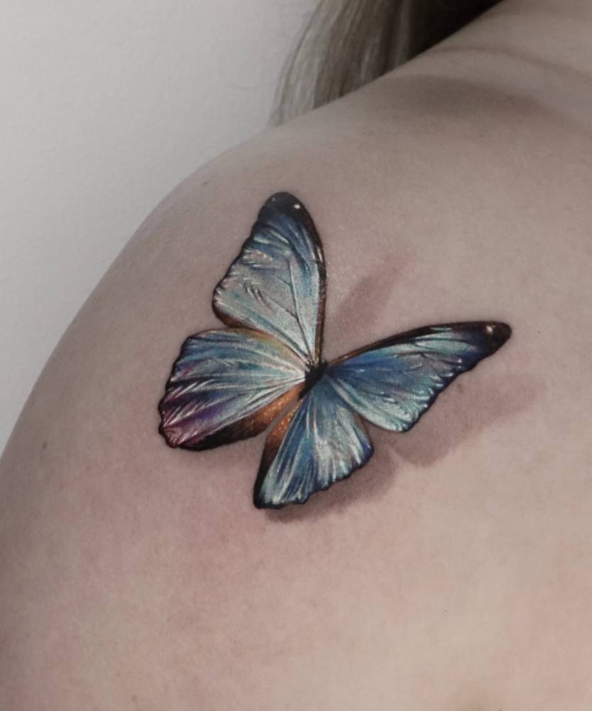 Blue butterfly tattoo in micro-realism located on the shoulder.