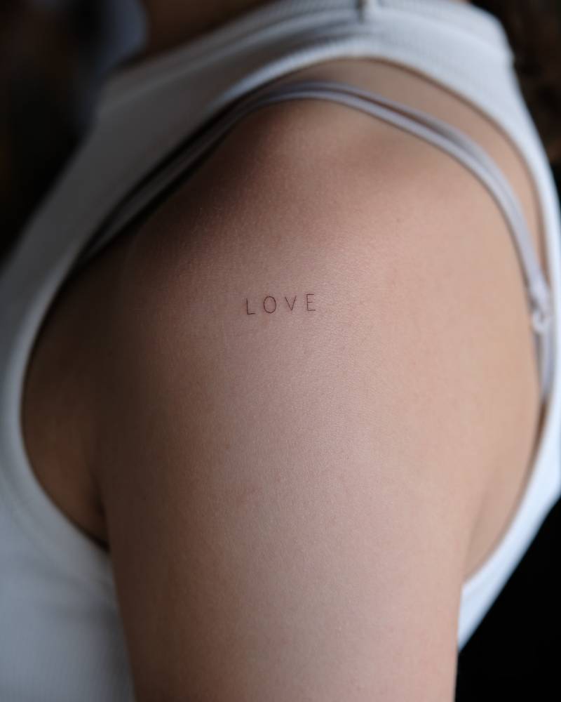 Lettering tattoo of the word "love" handwritten on the shoulder.