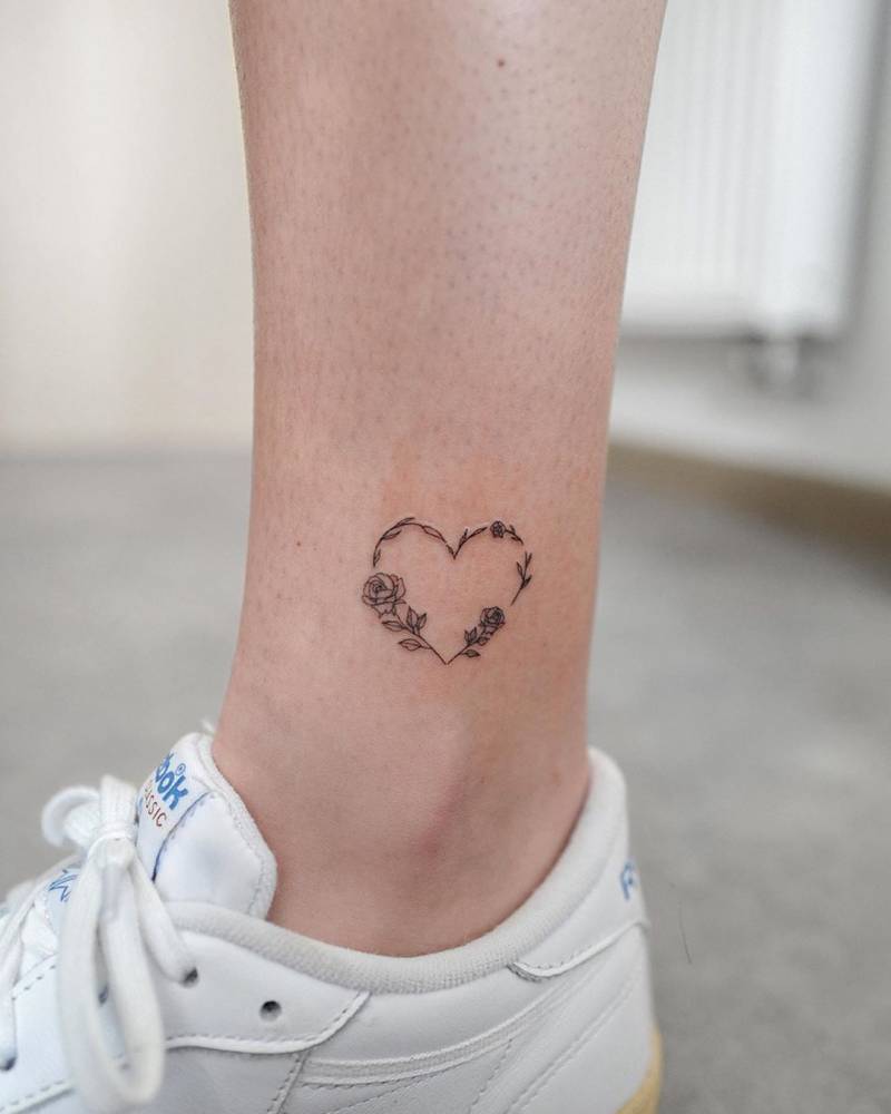 Flower heart tattoo located on the ankle, illustrative style.