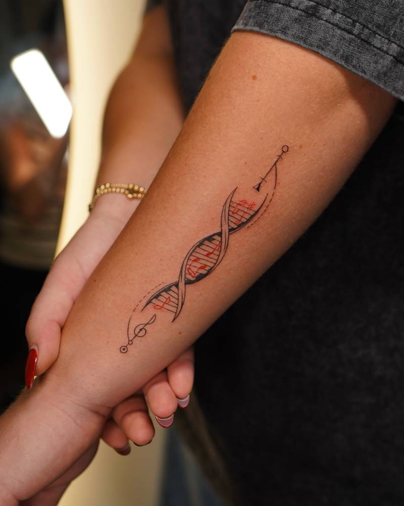 DNA tattoo in illustrative style located on the forearm.