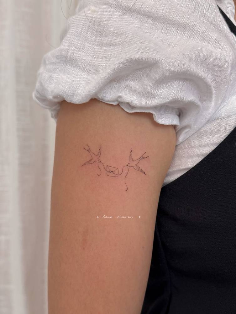 Swallows and love letter tattoo in fine line style located on the upper arm.