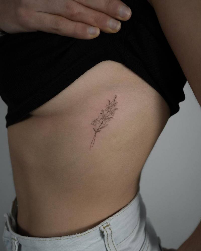 Fine line daisies & forget me nots tattooed on the side boob.