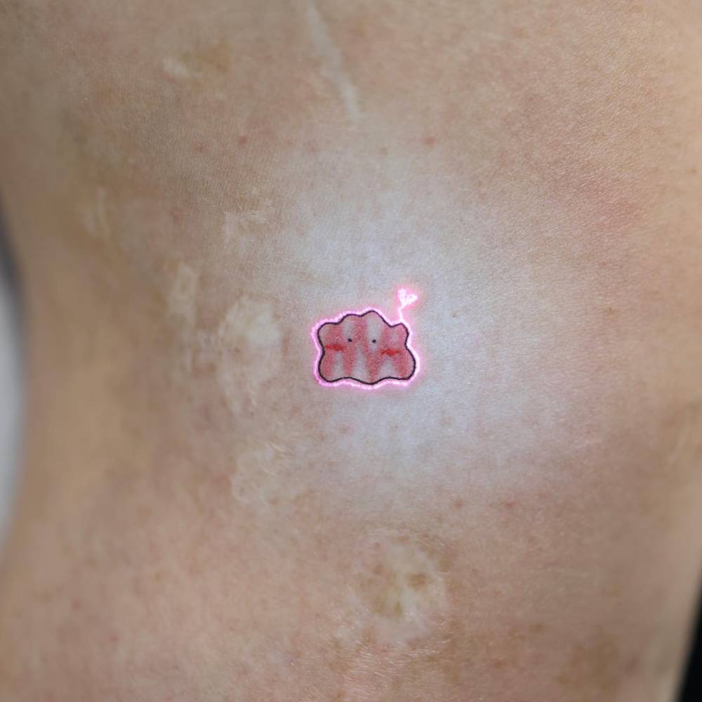 UV ink Ditto tattoo located on the upper arm, cartoon style.