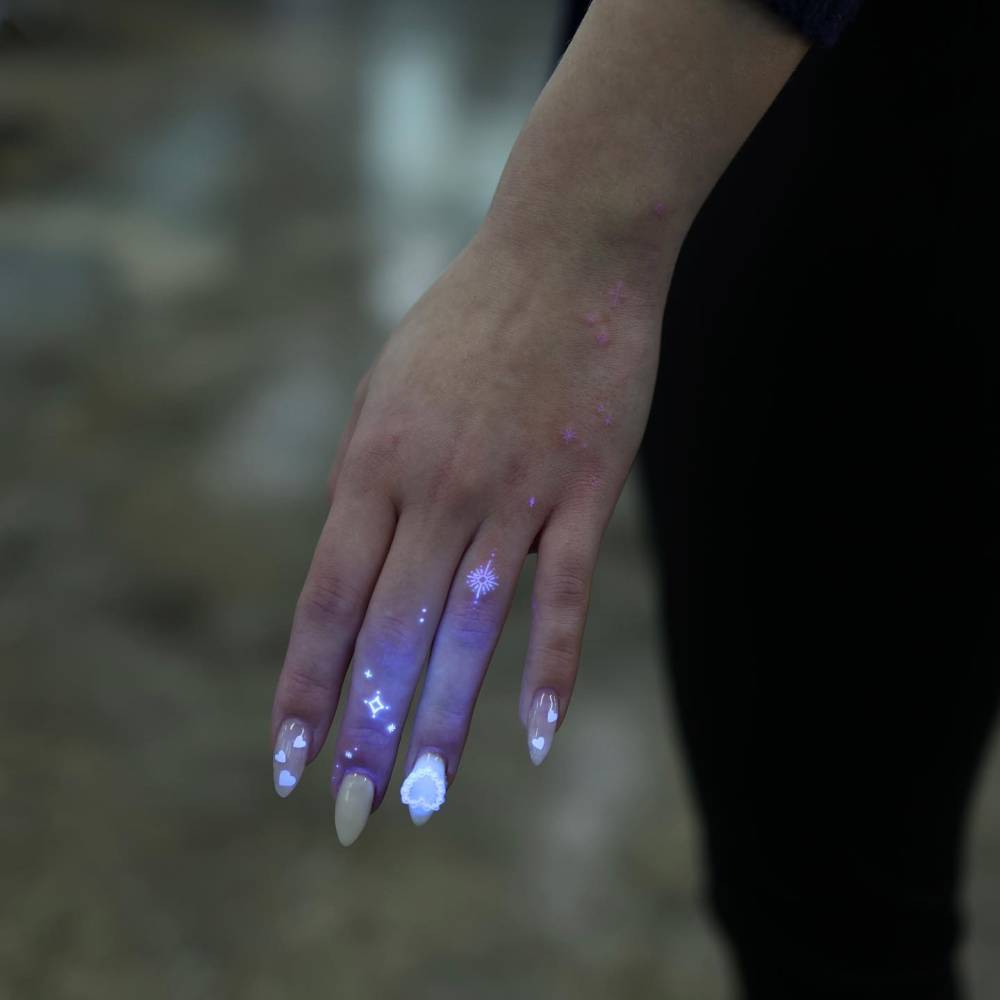 Sparkling stars tattoo in UV ink located on the fingers.