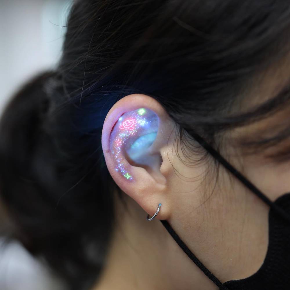 UV ink minimalistic galaxy tattoo located on the ear.