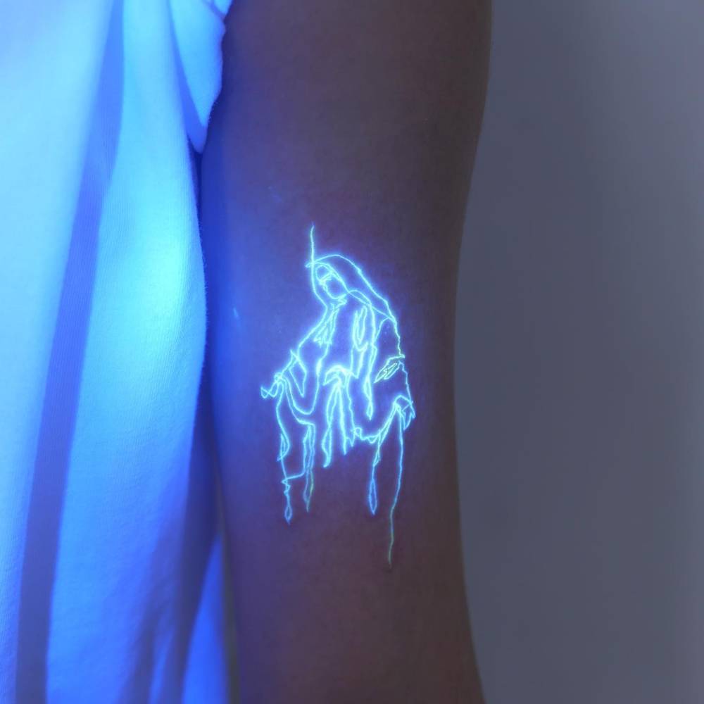 UV ink Virgin Mary tattoo located on the bicep.