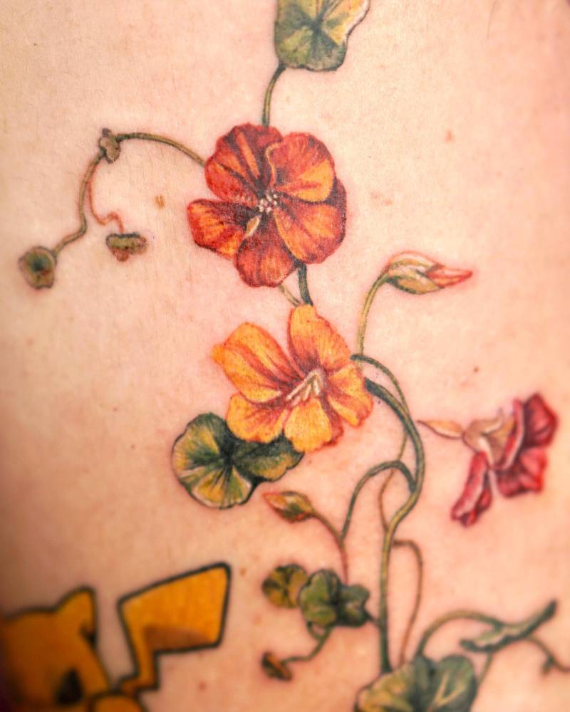 Nasturtium flowers tattooed on the upper arm, done in watercolor style.