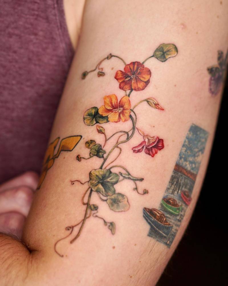 Nasturtium flowers tattooed on the upper arm, done in watercolor style.
