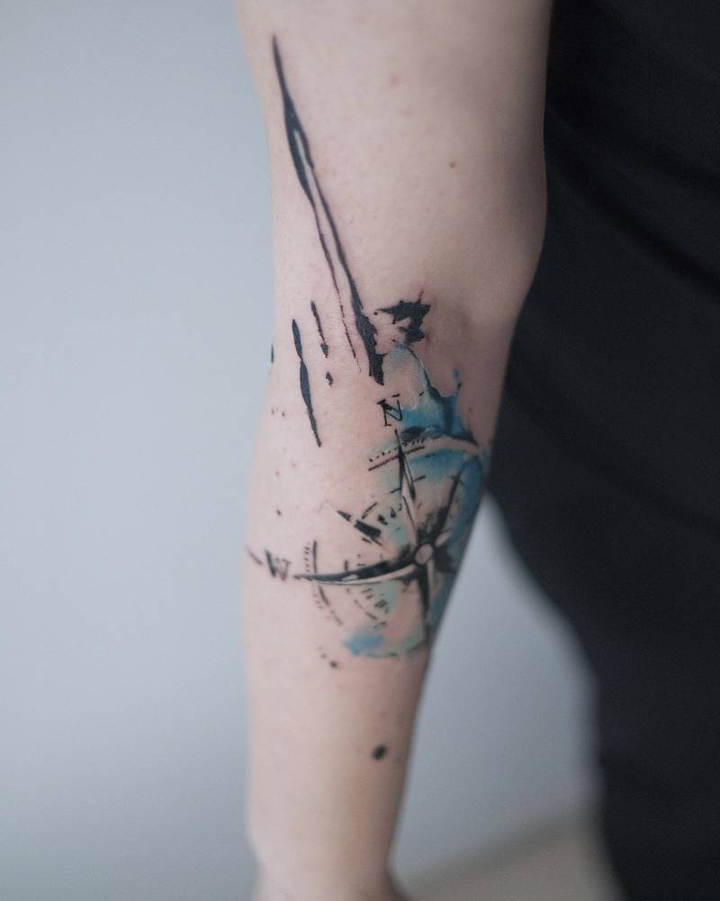 Watercolor style compass tattoo located on the arm.