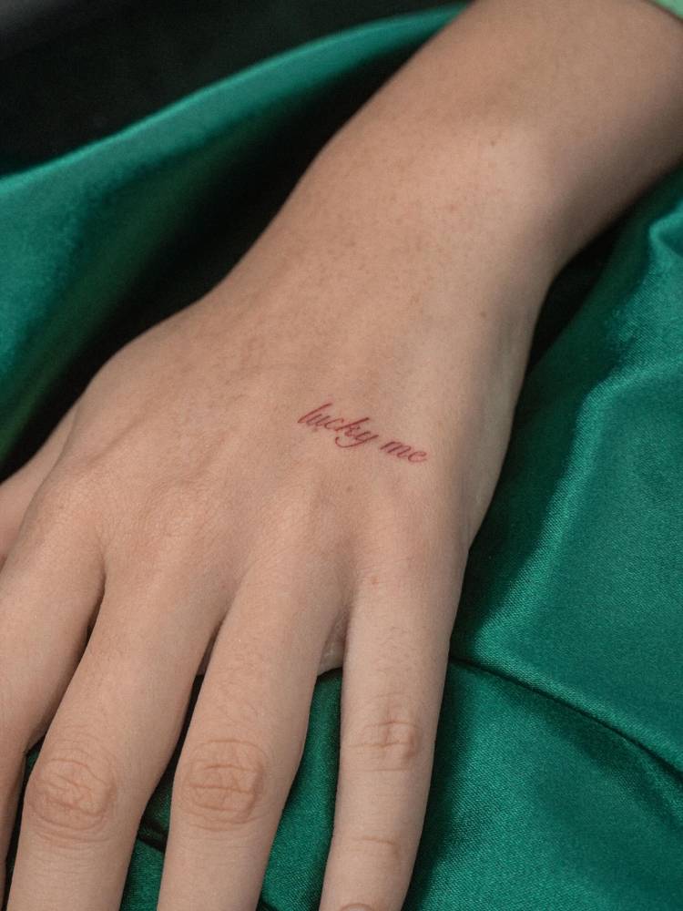Script font "lucky me" lettering tattoo located on the hand.