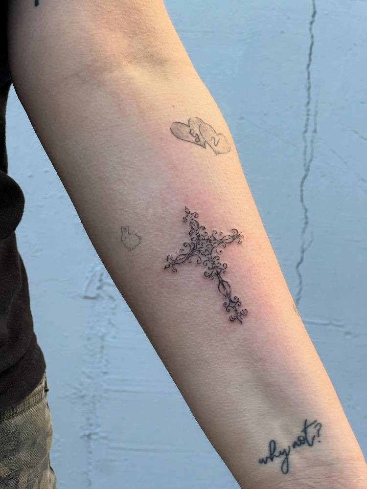 Ornamental cross tattoo located on the inner forearm.