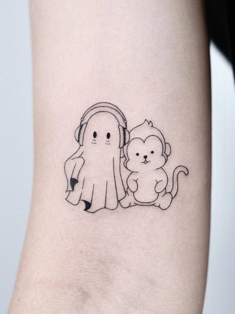 Ghost and monkey tattoo located on the bicep, cartoon style.