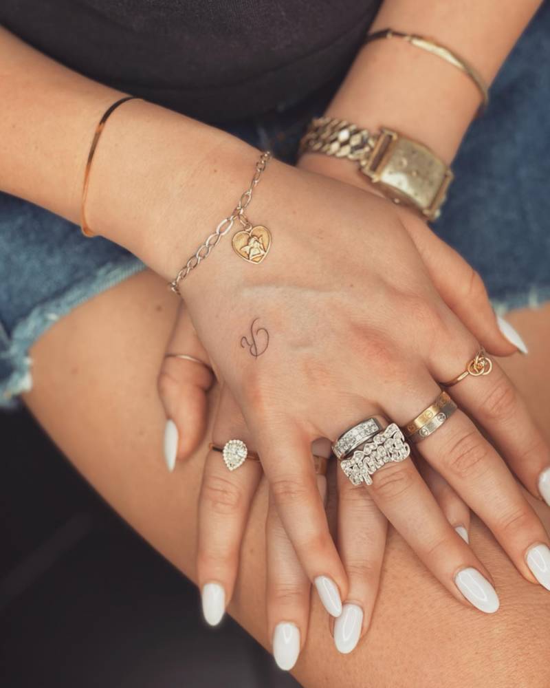 Tiny letter "R" tattoo located on the hand.