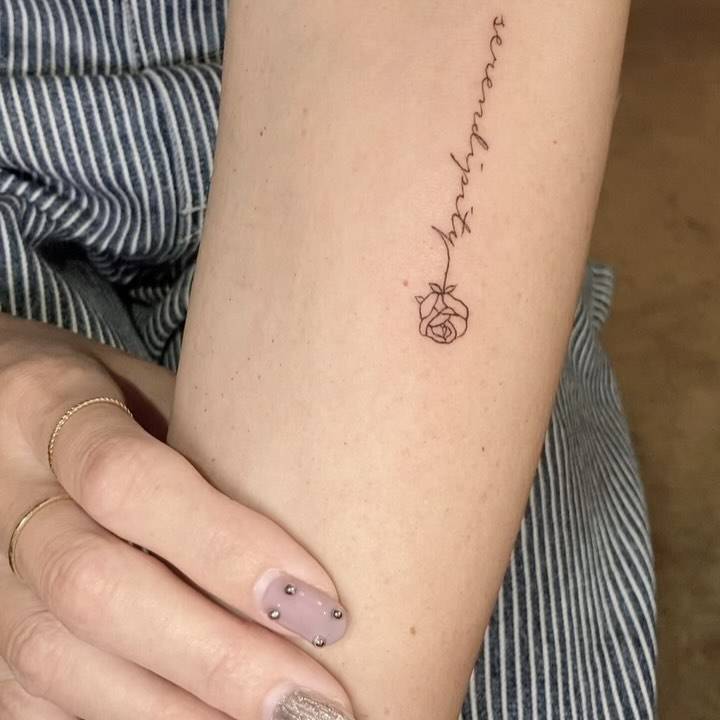 Word "serendipity" and rose tattoo located on the inner forearm.