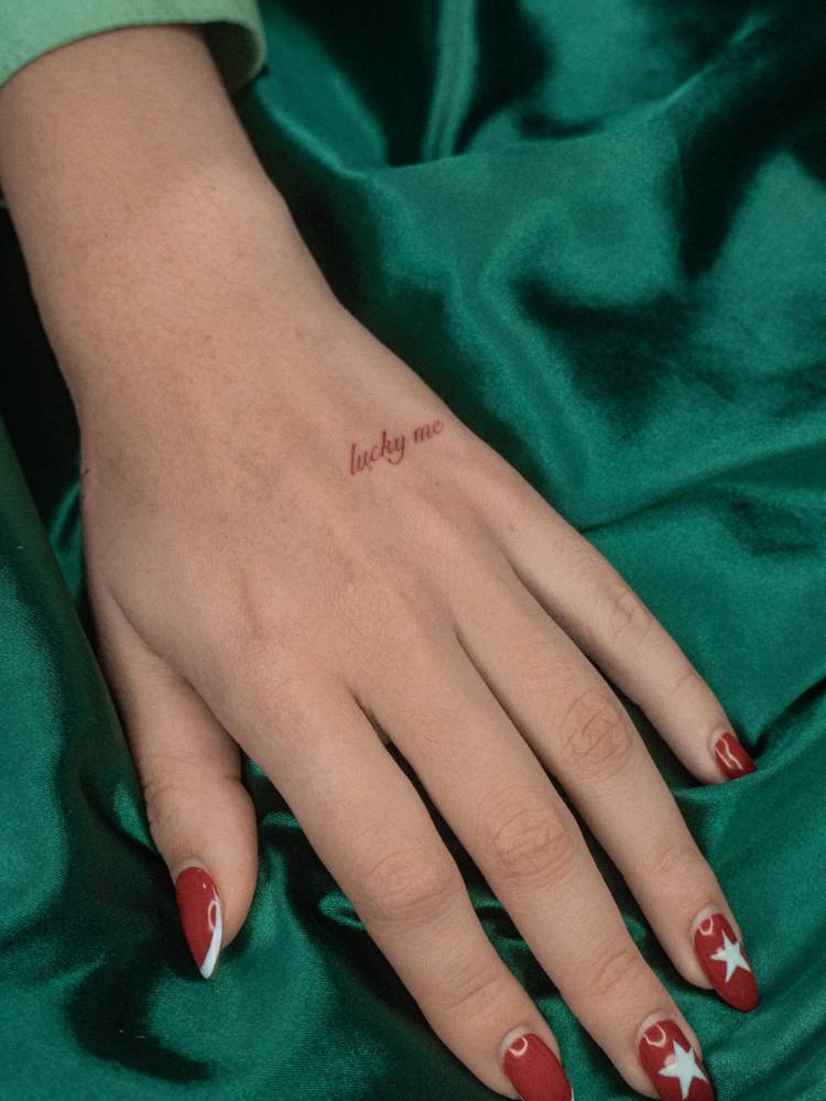 Script font "lucky me" lettering tattoo located on the hand.