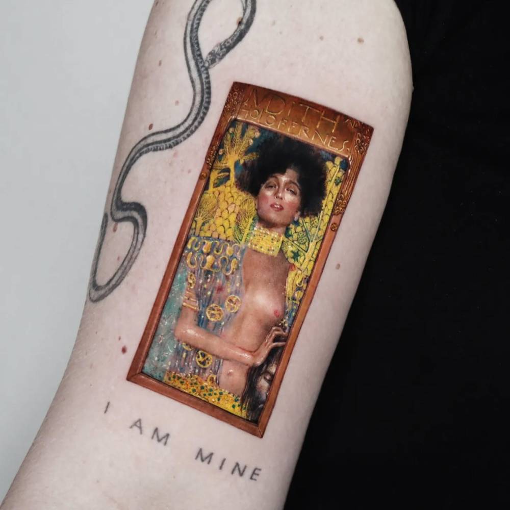 'Judith I' tattoo located on the bicep, contemporary style.