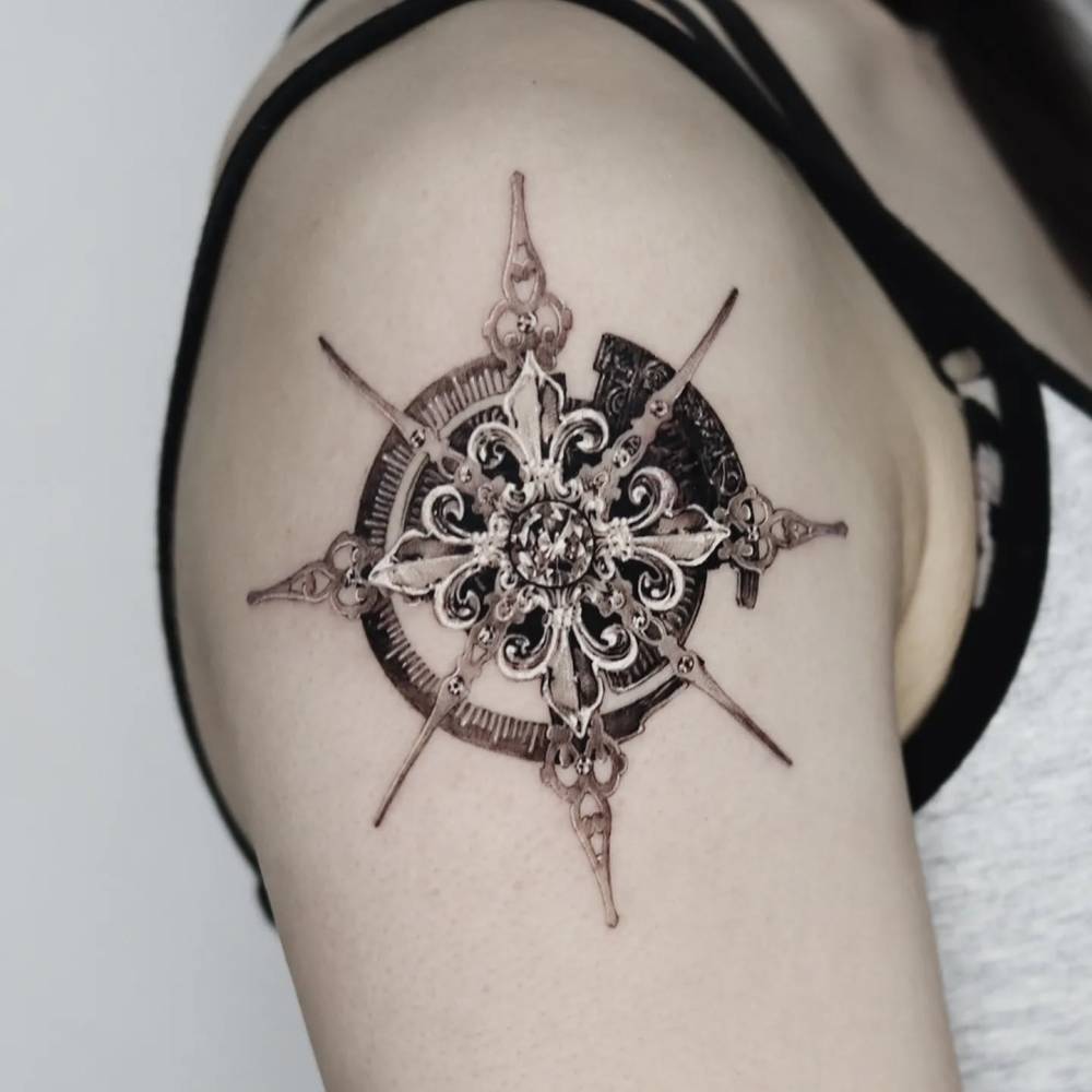 Compass tattoo in black and grey style done on the upper arm.