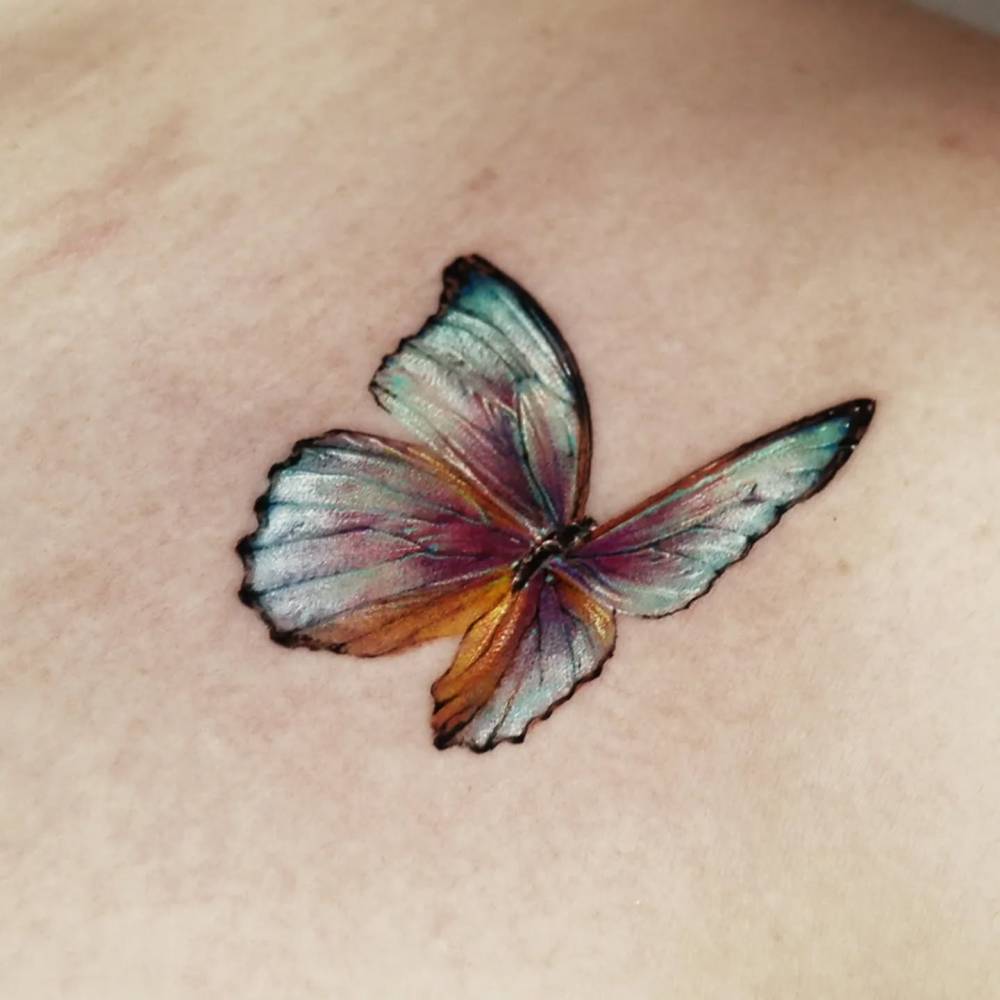 Blue butterfly tattoo in micro-realism placed on the collarbone.