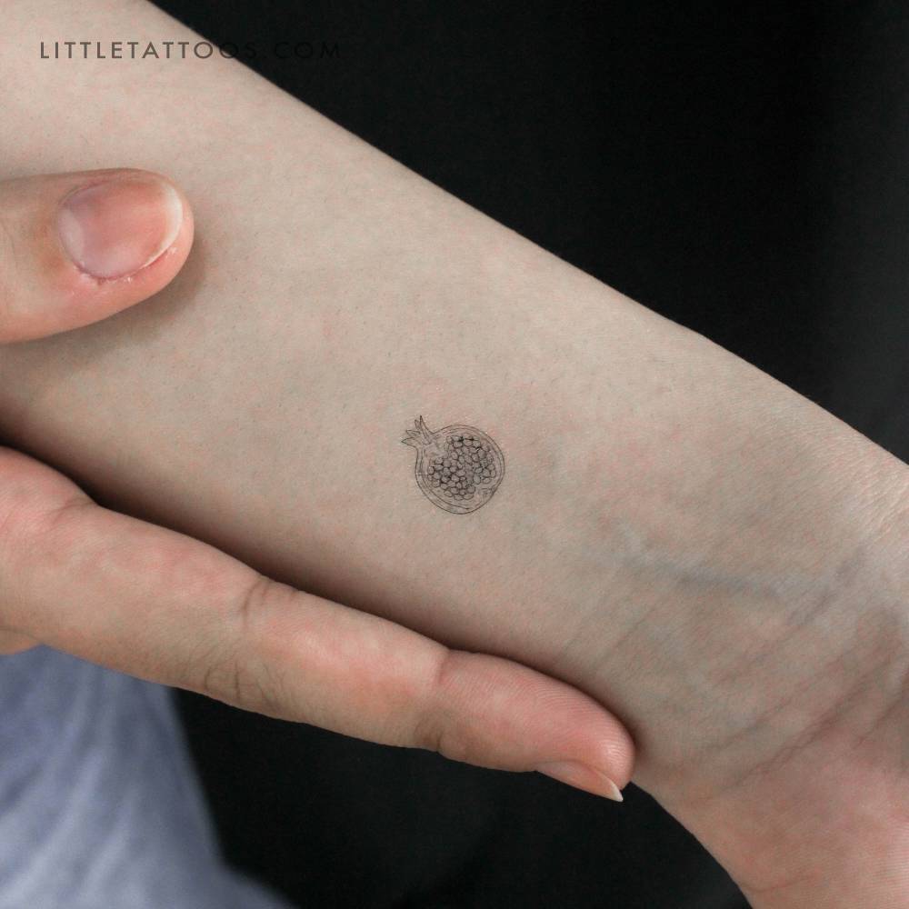 Tiny pomegranate temporary tattoo located on the wrist.